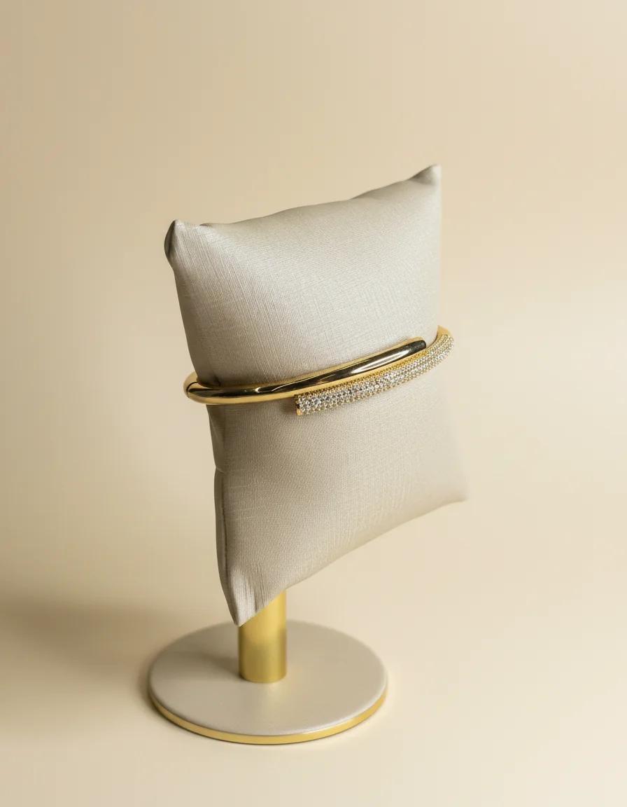 Bracelete dourado com barra cravejada em expositor de almofada e base dourada