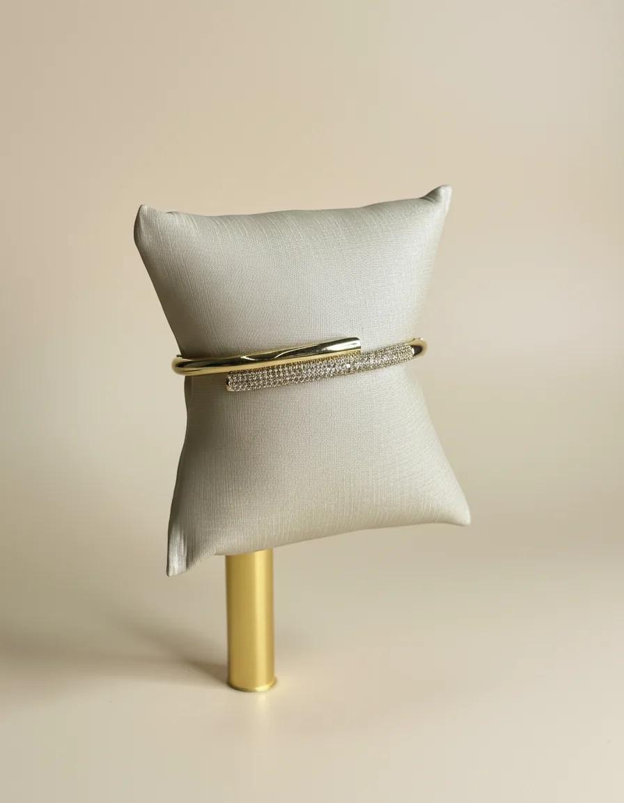Bracelete dourado visto de frente, com a barra cravejada sobre o tubo polido