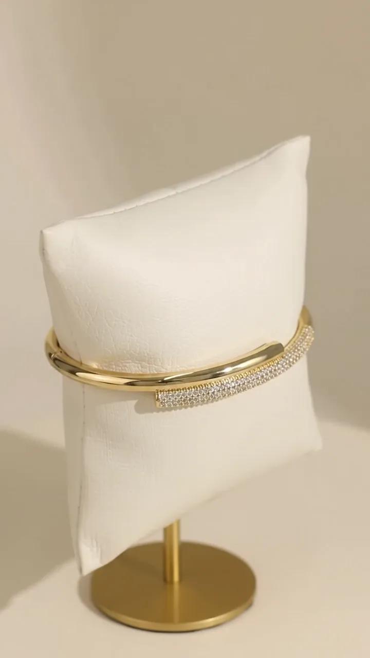 Bracelete banhado a ouro com barra cravejada, apoiado em almofada off-white